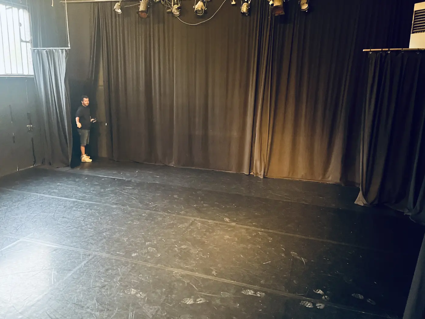 Le plateau de La Fonderie entre des rideaux noirs, sous une rangée de projecteurs&nbsp;; un homme se tient près du rideau, à gauche.